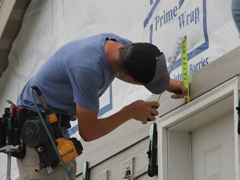 the kingdom builders employee measuring siding on home