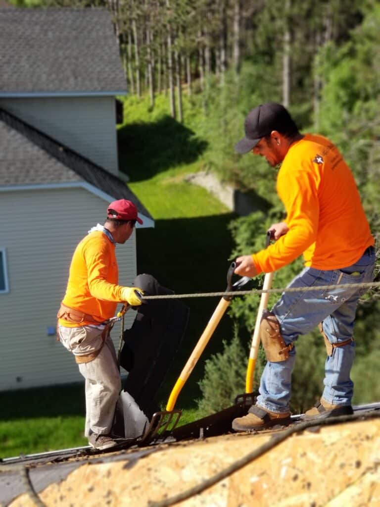 Roof installers roped off on roof removing shingles in Coon Rapids, MN