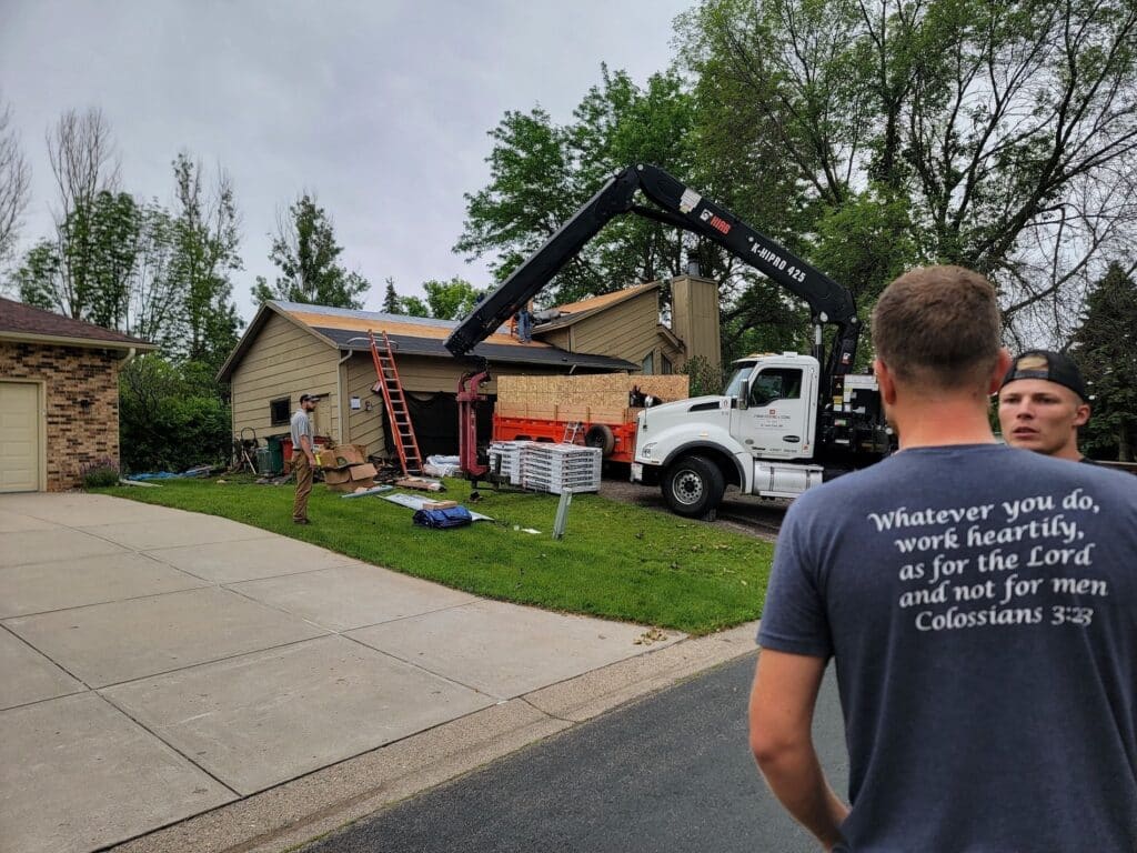 Photo of the house after cedar shake removal and the boom truck in the driveway loading the roof with the new materials.